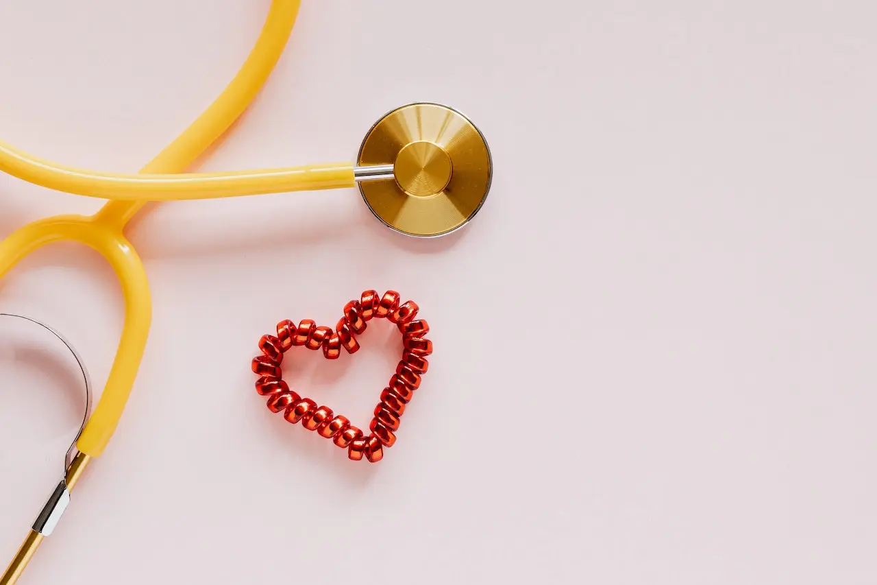 Yellow stethoscope and red beaded heart shape on pink background