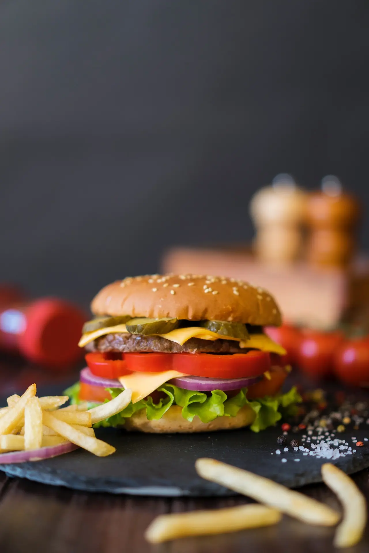 Cheeseburger with fries, tomatoes, and pickles on dark surface