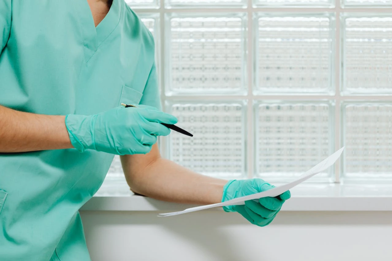 Healthcare provider in teal scrubs reviewing medical test results at a bright clinic window