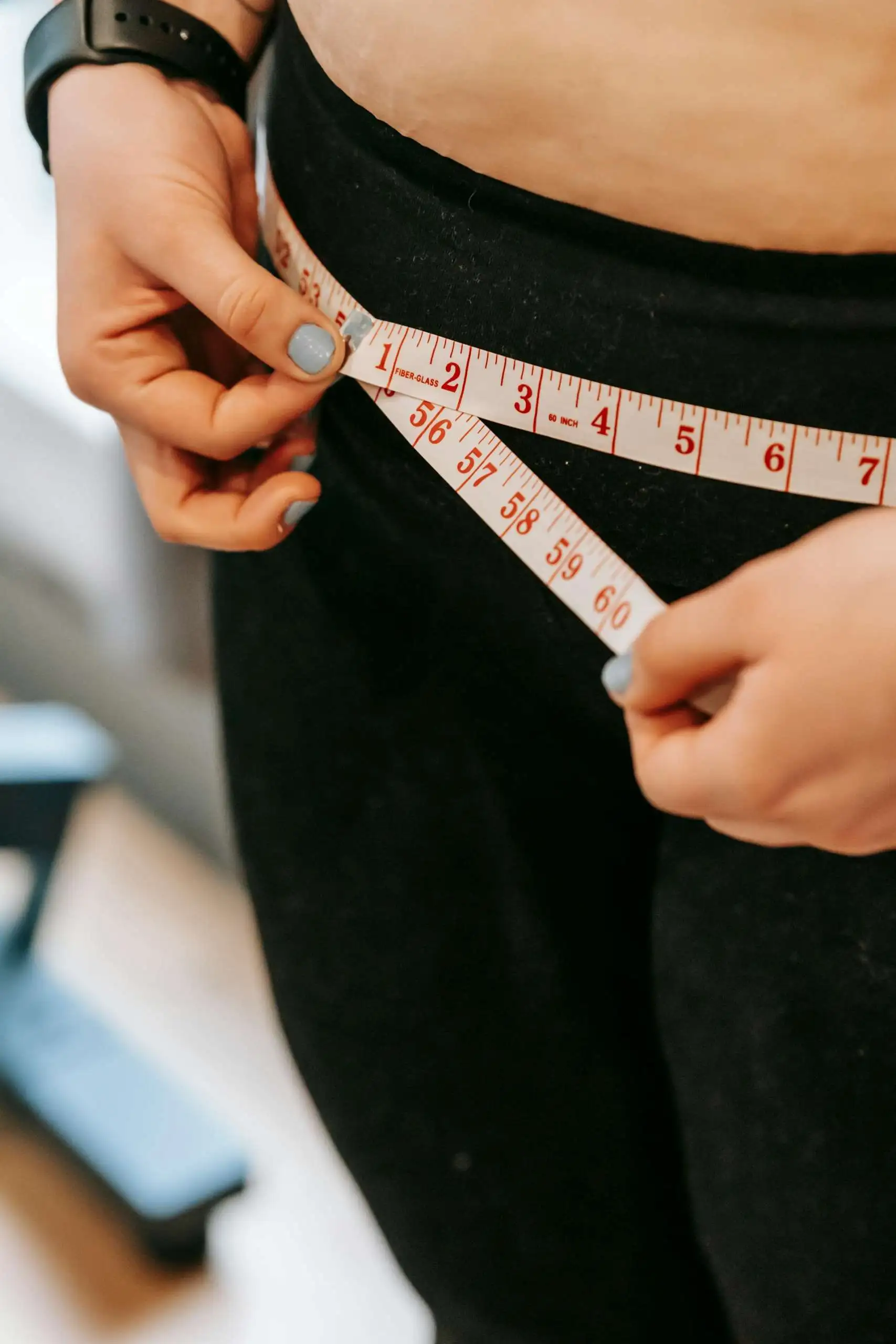 Person measuring waist with measuring tape while wearing black athletic shorts