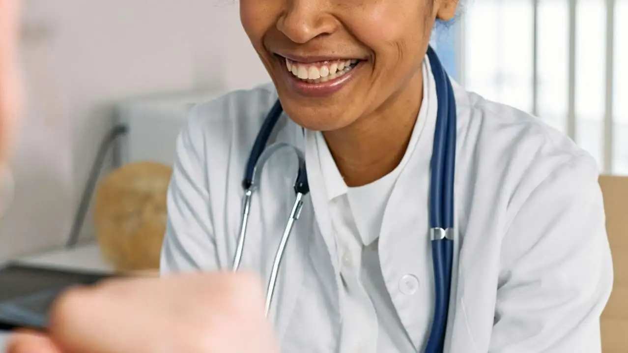 Primary care physician in white coat with stethoscope speaking with patient