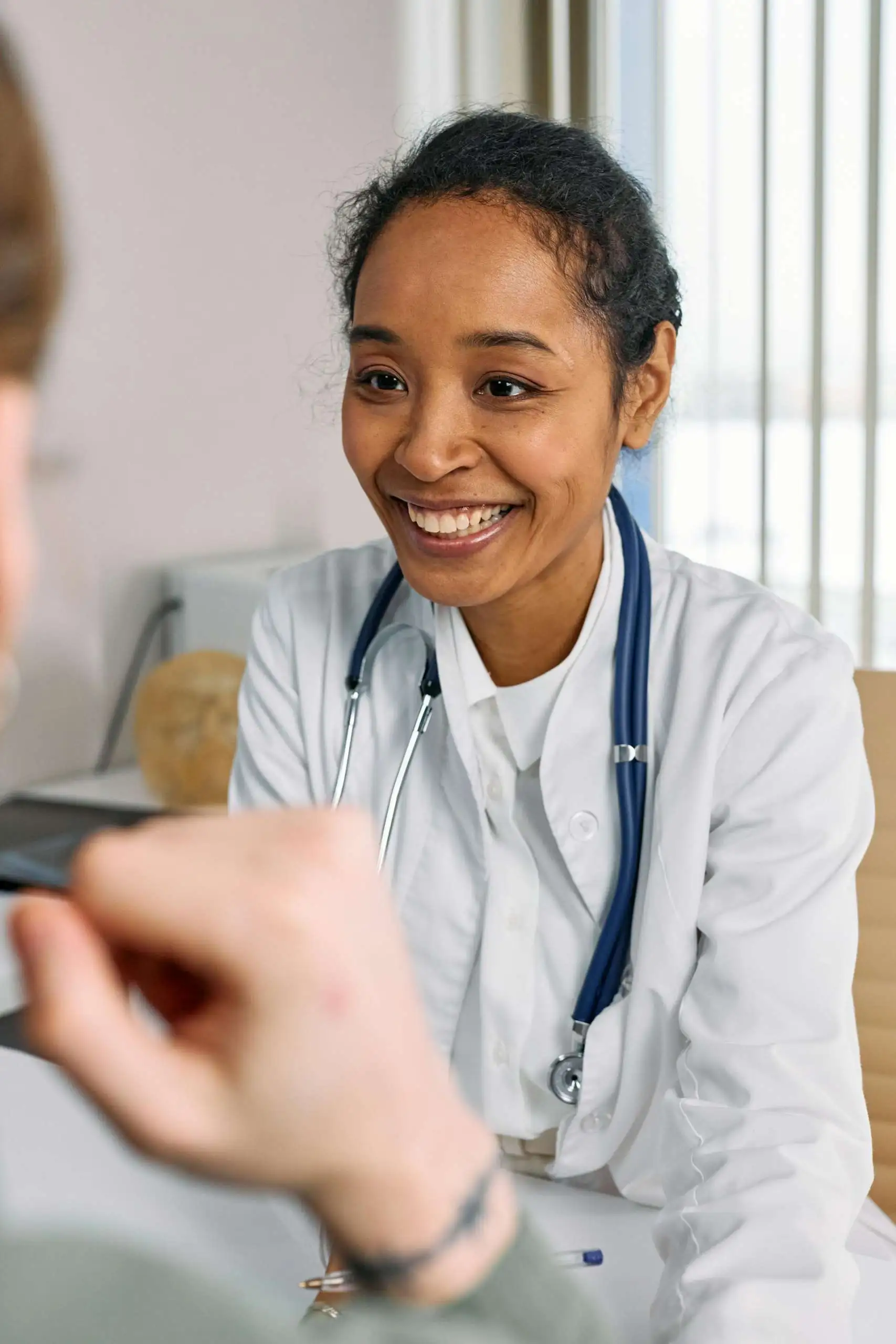 Primary care physician in white coat with stethoscope speaking with patient