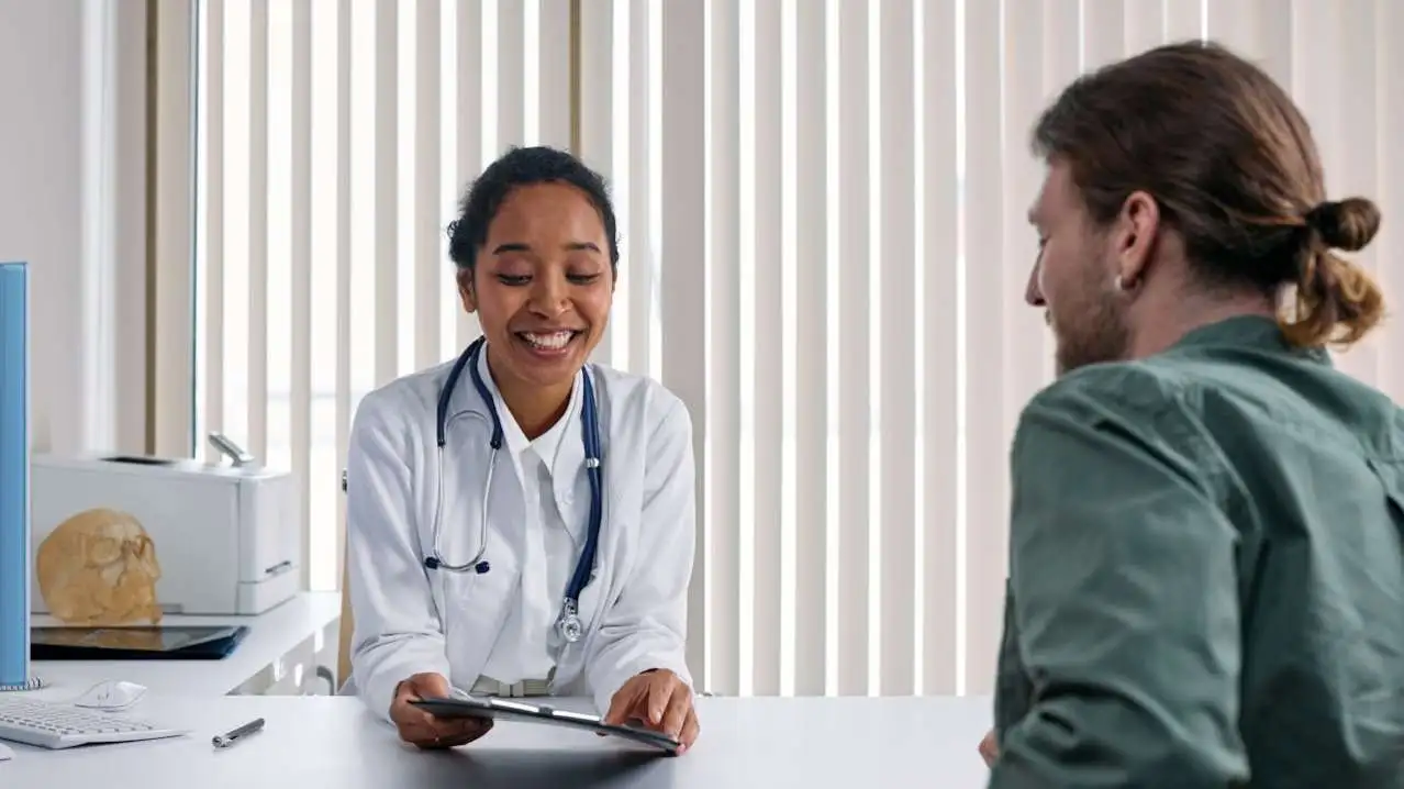 Female physician reviewing tablet with male patient across desk in clinical office