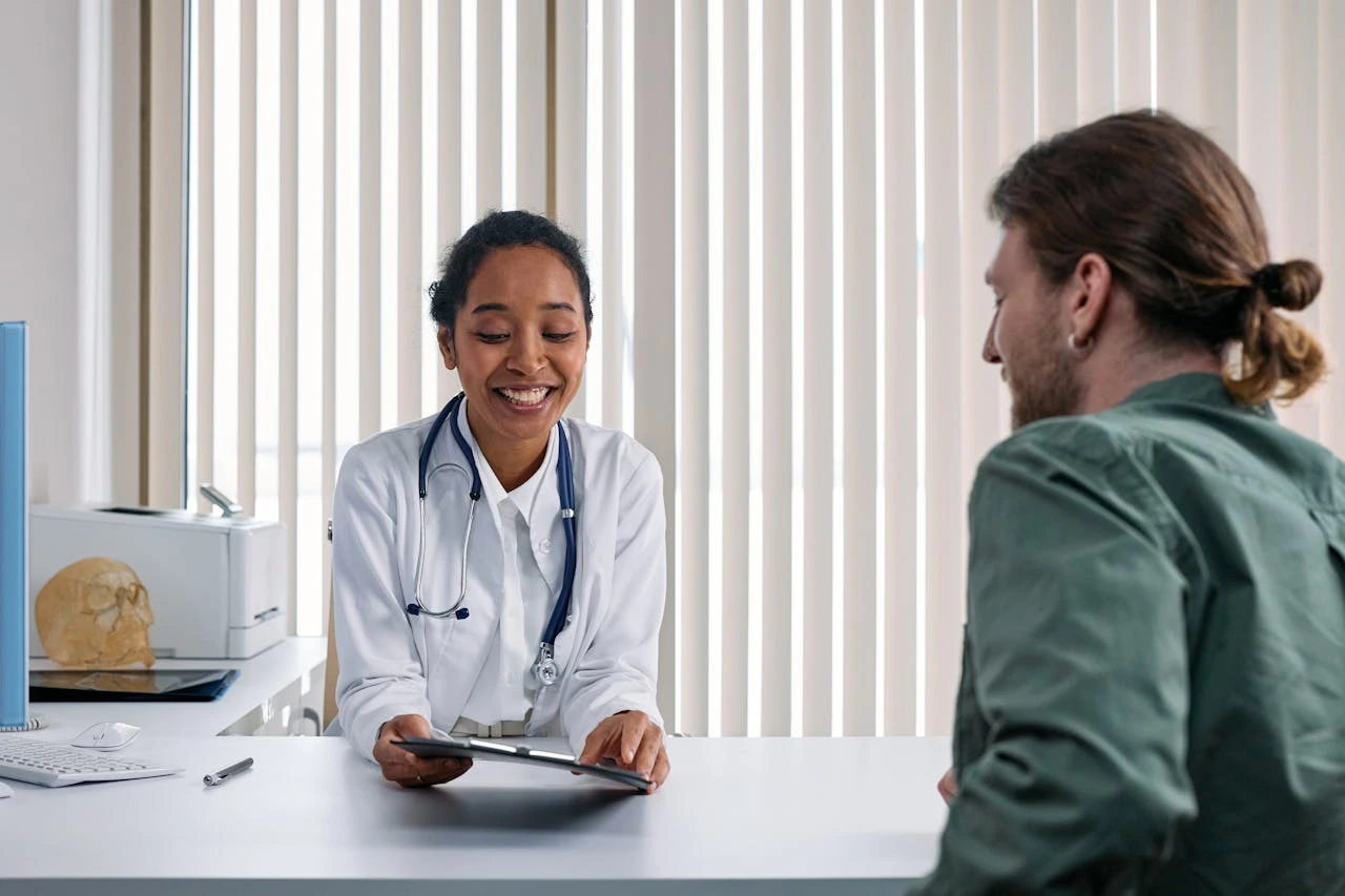Female physician reviewing tablet with male patient across desk in clinical office
