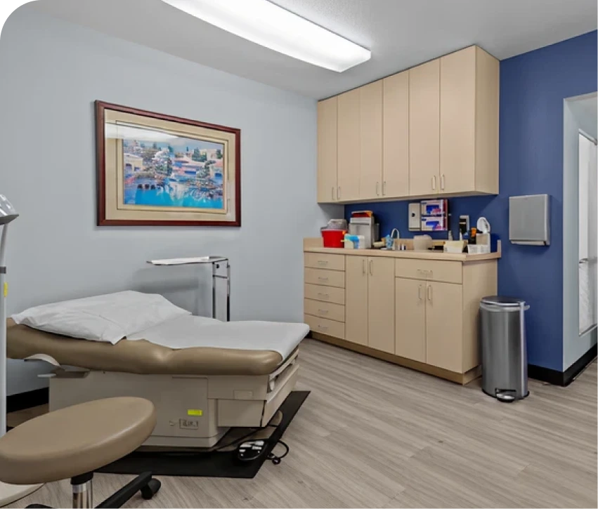 Modern medical exam room with examination table, cabinetry, and framed artwork on blue wall